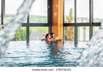 Young adult couple spending time together and relaxing in indoor swimming pool at hotel resort.