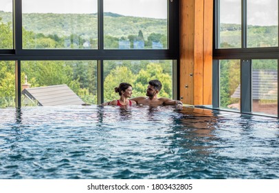 Young adult couple spending time together and relaxing in indoor swimming pool at hotel resort.	