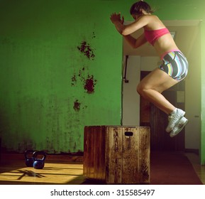 Young adult crossfit girl jumping on box in gym club.