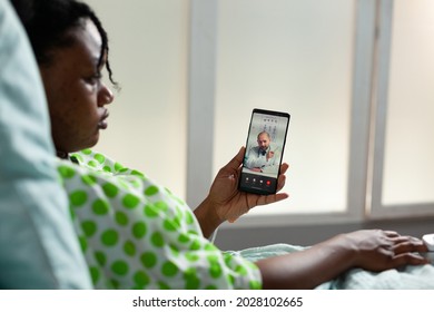 Young Adult With Disease Using Telemedicine On Smartphone Talking To Doctor About Healing Treatment. African American Patient On Video Call Consultation While Sitting In Hospital Ward