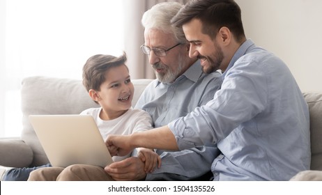 Young adult father and old senior grandfather teach little child son grandson using laptop sit on sofa, happy three 3 age multi generation men family spend time online with computer together at home - Powered by Shutterstock