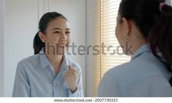 Young adult female asia people self love cheer up\
pep talk before job interview deep breathe inhale standing look in\
front of mirror smile at home in mental health care or work career\
stress relief.