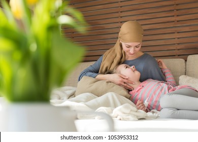 Young Adult Female Cancer Patient Spending Time With Her Daughter At Home, Relaxing On The Couch. Cancer And Family Support Concept.