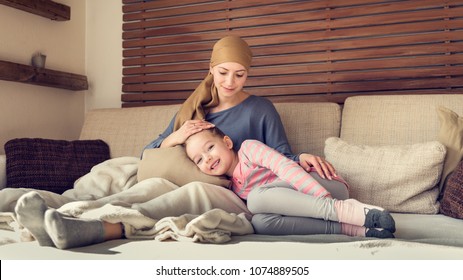 Young Adult Female Cancer Patient Spending Time With Her Daughter At Home, Relaxing On The Couch. Cancer And Family Support Concept.