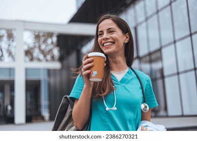 The young adult female nurse drinks her coffee as she arrives to work at the hospital. A young adult female nurse arrives for a shift in a hospital. She is wearing medical scrubs - Powered by Shutterstock