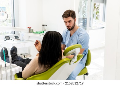 Young Adult Female Patient Sitting On A Dental Chair And Having A Conversation With Her Dentist. Preparing Patient For A Treatment. Rear View Of The Patient, Focus On A Male Dentist.