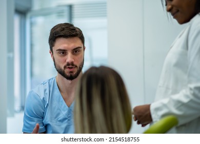 Young Adult Female Patient Sitting On A Dental Chair And Having A Conversation With Her Dentist. Preparing Patient For A Treatment. Rear View Of The Patient, Focus On A Dentist.