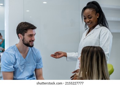 Young Adult Female Patient Sitting On A Dental Chair And Having A Conversation With Her Dentist. Preparing Patient For A Treatment. Focus On A Male And Female Dentist, Rear View Of The Patient.