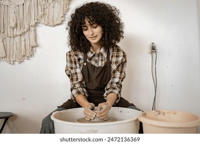 Young adult female potter using a pottery wheel to sculpt ceramic dishes in an art studio environment. - Powered by Shutterstock