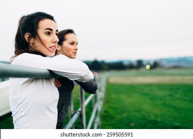 Young Adult Female Runners Leaning On Fence Post In Country Looking