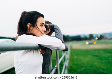 Young Adult Female Runners Leaning On Fence Post In Country Looking