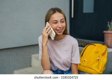 Young Adult Female Sitting In Front Steps Of Her Home Talking On Mobile Phone