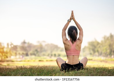 Young Adult Female In Sportswear Doing Yoga In The Park Outdoor, Healthy Woman Sitting On Grass And Meditation With Lotus Pose In Morning. Wellness, Fitness, Exercise And Work Life Balance Concepts