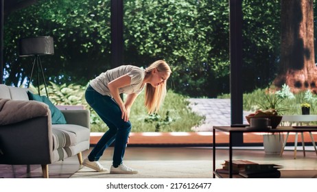 Young Adult Female Standing Up From A Couch At Home And Experiencing Discomfort In A Result Of Leg Trauma Or Arthritis. Joint And Knee Injury Concept. Massaging The Muscles To Ease The Pain.