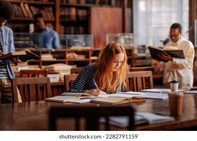 A young adult female student is sitting at the table in the library, studying for her upcoming exams. - Powered by Shutterstock