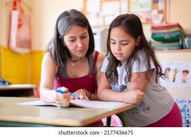 Young Adult Female Teacher Helping A Primary School Pupil In Class To Learn A Lesson. Concept Of Education And Development In Children.