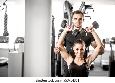 Young adult fitness couple. Woman doing chest and shoulder dumbbell  press on bench with personal coach assisting her and giving instructions. - Powered by Shutterstock