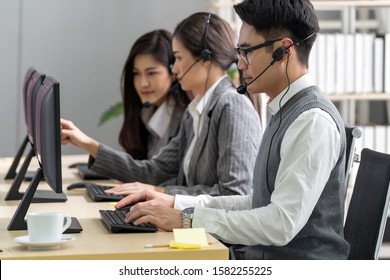 Young adult friendly and confidence operator man agent with headsets working in a call center with his colleague team working as customer service and technical support workplace in background. - Shutterstock ID 1582255225