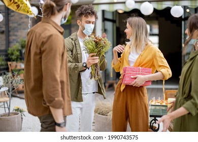 Young Adult Friends Gathering For Birthday Party At The Backyard Of Country House. Wearing Face Masks And Greet With Social Distance, New Normal During Pandemic