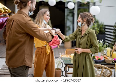 Young Adult Friends Gathering For Birthday Party At The Backyard Of Country House. Wearing Face Masks And Greet With Social Distance, New Normal During Pandemic