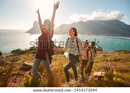 Young adult friends hiking single file uphill celebrate reaching a summit, full length, side view