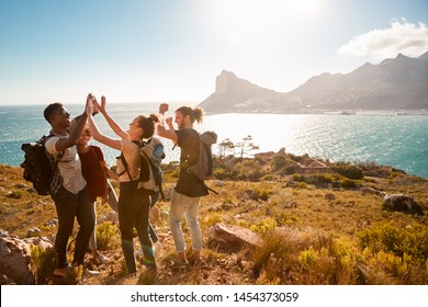 Young adult friends on a hike celebrate reaching a summit near the coast, full length, side view
