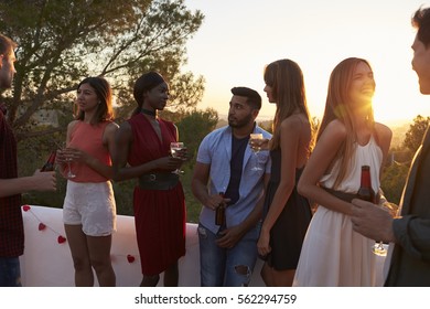 Young Adult Friends Talk At A Party On A Rooftop At Sunset