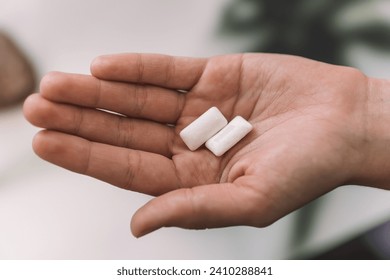 Young adult girl hand pouring white chewing gum pads from green pack in opened palm on blue table background. Pastel color. Closeup. Point of view shot. top view,