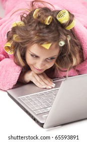 Young Adult Girl In Pink Dressing Gown And With Hair Rollers Lying With Laptop