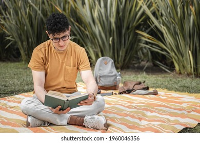 Young Adult Good Looking Caucasian Style Boy Man Relaxed Outdoor In A Spring Day Wearing Brown And Greay Clothes Reading Listening To Music Being Happy Chilling On Green Grass In A Sunn Day