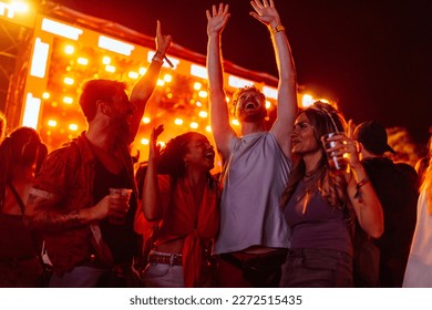 A young adult group of friends are at a music festival in the summer night dancing and singing to their favorite songs and having beer.