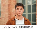 Young adult guy at academy. Individual portrait of a serious schoolboy looking at camera standing at high school. Teenage thoughtful male student staring front. Pensive man at university campus. High