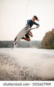young adult guy in wetsuit and vest jumps spectacularly on wakeboard above the water with splashes