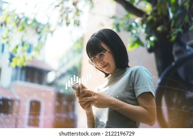 Young adult happy asian woman wear eyeglasses using mobile phone trade crypto cion and nft for money profit with digital graph. Poeple investment trend in metaverse concept. - Shutterstock ID 2122196729