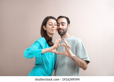 Young Adult Happy Couple Showing Heart-shape With Fingers. Love, Care. Mixed Race, Brown Hair. Attractive People, Closeup Portrait. Creative Studio Shot, Commercial, Advertising Concept