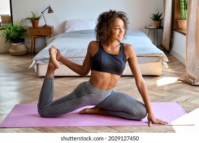 Young adult happy fit slim healthy African American ethnic woman wearing sportswear stretching sitting in yoga pose on mat at home in bedroom, doing fitness morning workout exercises training. - Powered by Shutterstock