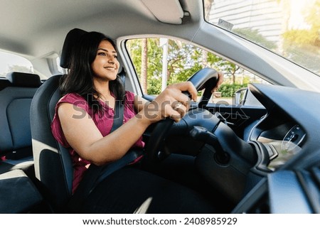 Young adult happy indian woman driving a car in the city. Rental car service concept