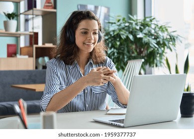 Young adult happy smiling Hispanic indian student wearing headphones talking on online chat meeting using laptop in university campus or at virtual office. College female student learning remotely. - Shutterstock ID 1959377737