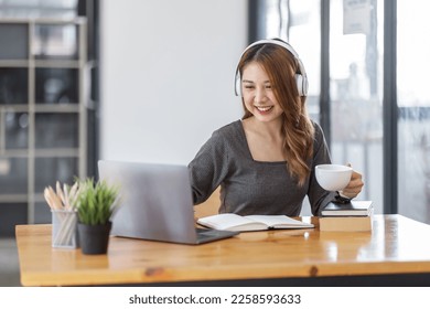 Young adult happy smiling Hispanic Asian student wearing headphones Online education using laptop in university campus or at virtual office. College female student learning remotely. - Shutterstock ID 2258593633