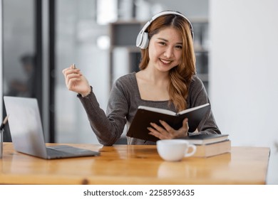 Young adult happy smiling Hispanic Asian student wearing headphones Online education using laptop in university campus or at virtual office. College female student learning remotely. - Shutterstock ID 2258593635