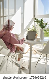 Young Adult Hipster Teen Girl School Student With Pink Hair Using Laptop Computer Sitting At Chair Kitchen Table Behind Glass Working Learning Online At Home Office Having Morning Breakfast. Vertical.