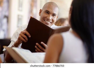 Young Adult Hispanic Couple Dining Out In Restaurant And Reading Menu. Horizontal Shape, Waist Up, Focus On Background