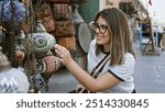 Young adult hispanic woman shopping at souq waqif in doha, inspecting a traditional lantern