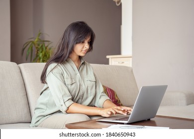 Young Adult Indian Professional Woman College Student, Remote Distanced Worker Using Laptop Computer Working Online At Home Office, Typing, E Learning In Internet Sitting On Couch In Living Room.