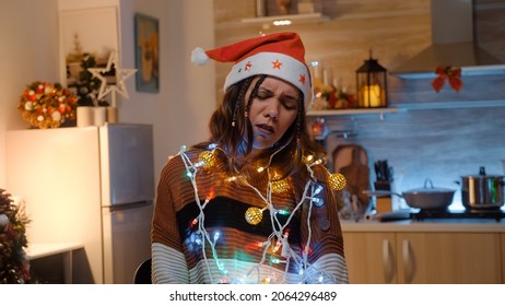 Young Adult With Knotted String Of Christmas Lights Tangled While Trying To Decorate Home For Winter Holiday. Festive Woman Preparing For Dinner Party Celebration With Friends And Family