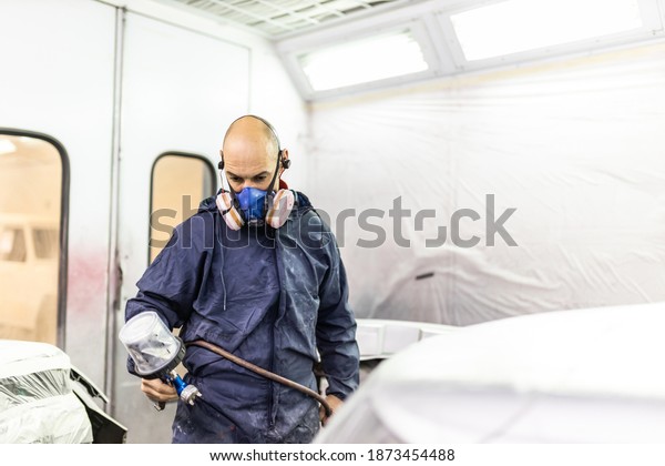 young adult male car painter, painting a car in
the paint booth of his
workshop