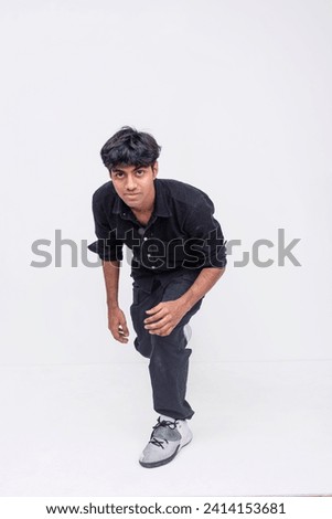 Young adult male crouching and looking at the camera with a serious expression, dressed in casual clothing.