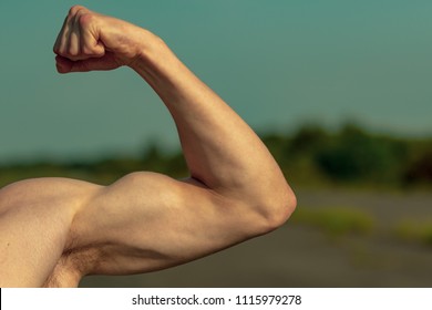 Young adult male flexing his bicep muscles shirtless on a warm summer's day