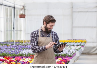 Young adult male garden worker in apron using digital tablet at greenhouse - Powered by Shutterstock