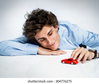 Young Adult Male Plays With Red Toy Car And Having Fun / Photos Of Immature Man Wearing  Blue Shirt Over Gray Background